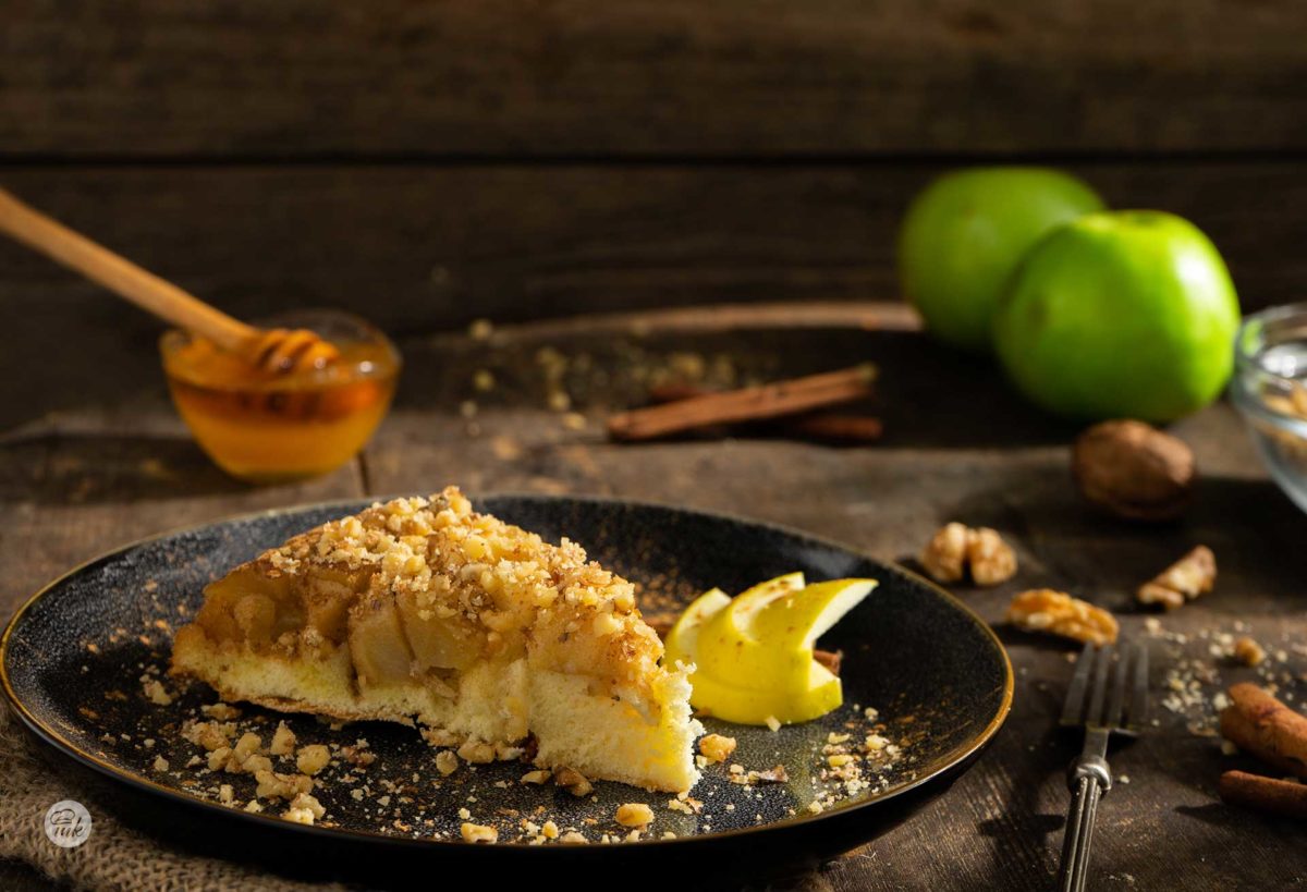 Ябълкова тортар сервирана в чиния с натрошени орехи, мед, ябълки на заден фон, снимано отстрани