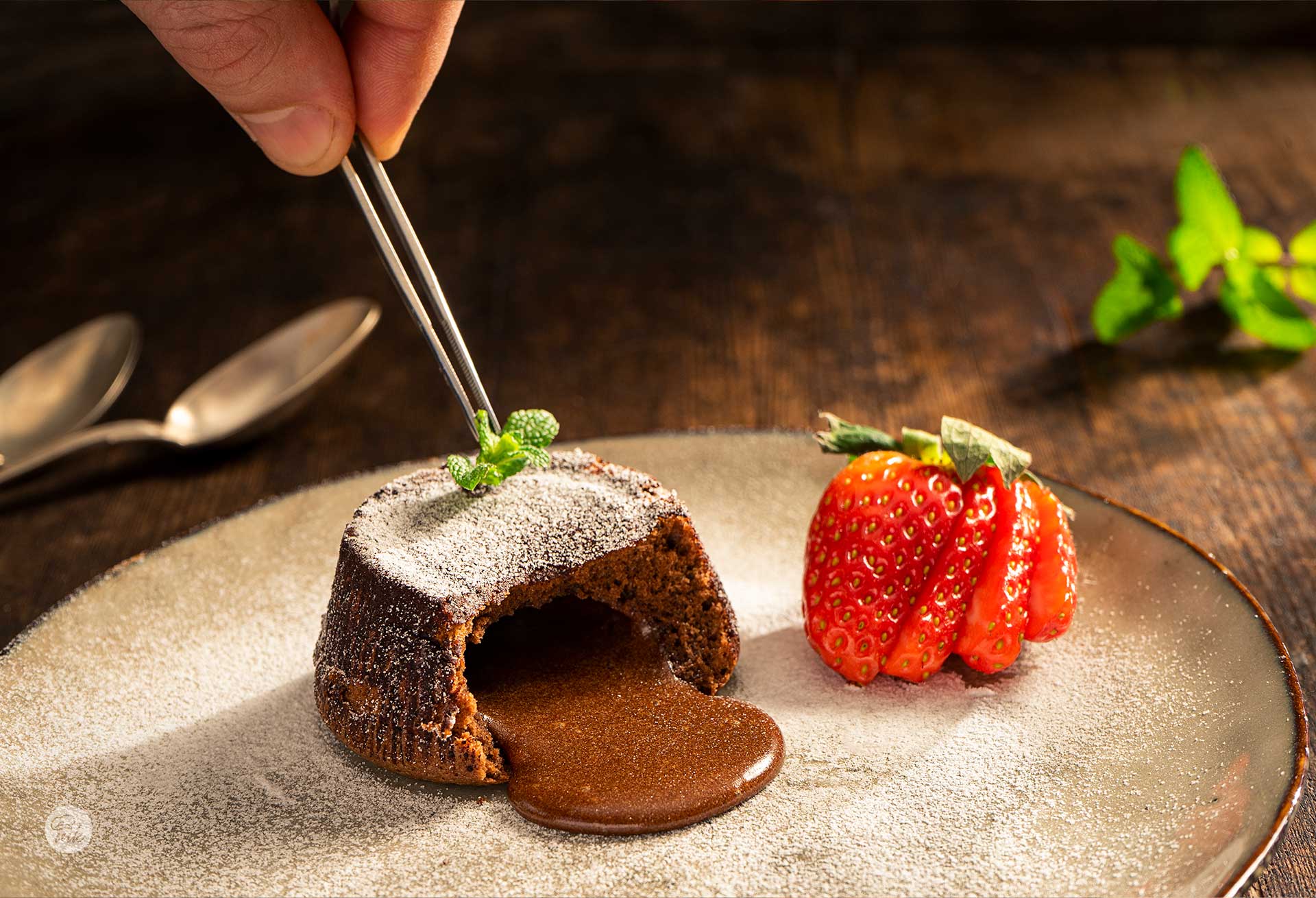 Шоколадово суфле, сервирано в чиния с пудра захар, ягоди и листенце мента, снимано отстрани