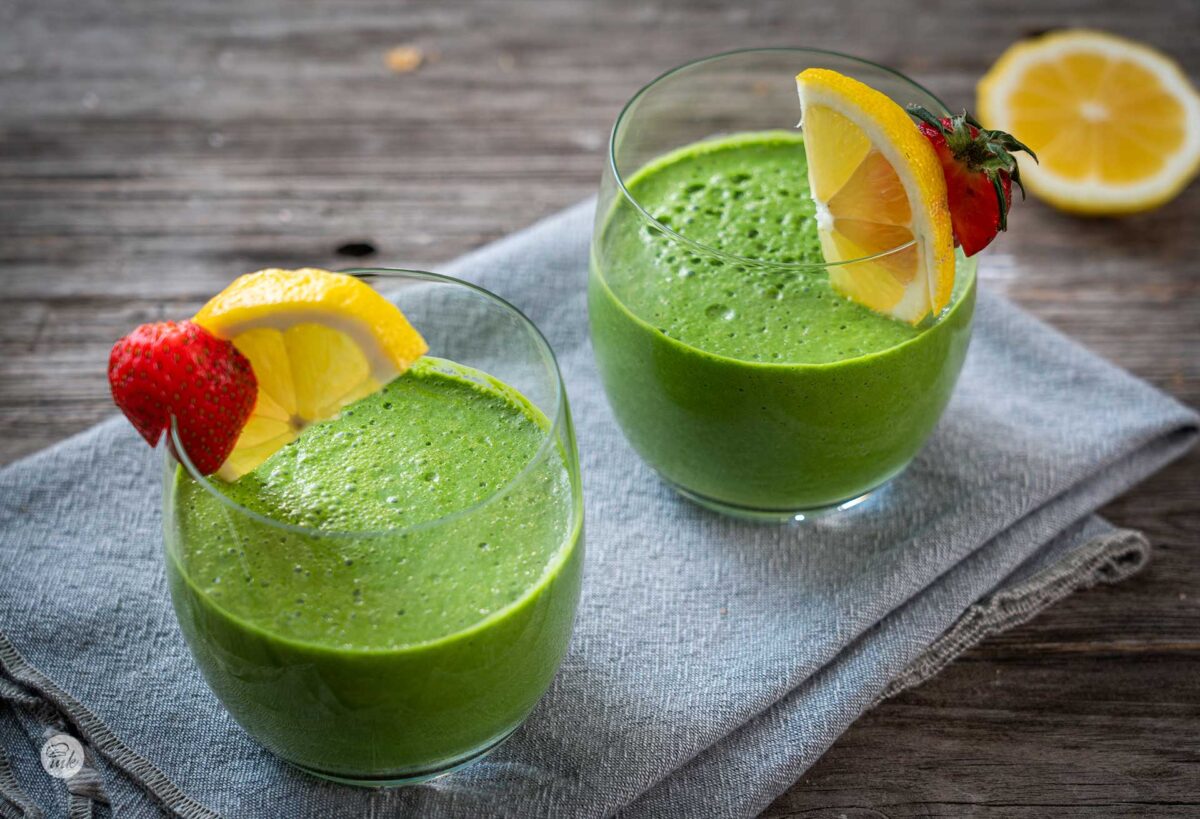 Две чаши зелено млечно смути, гарнирани с лимон и ягода