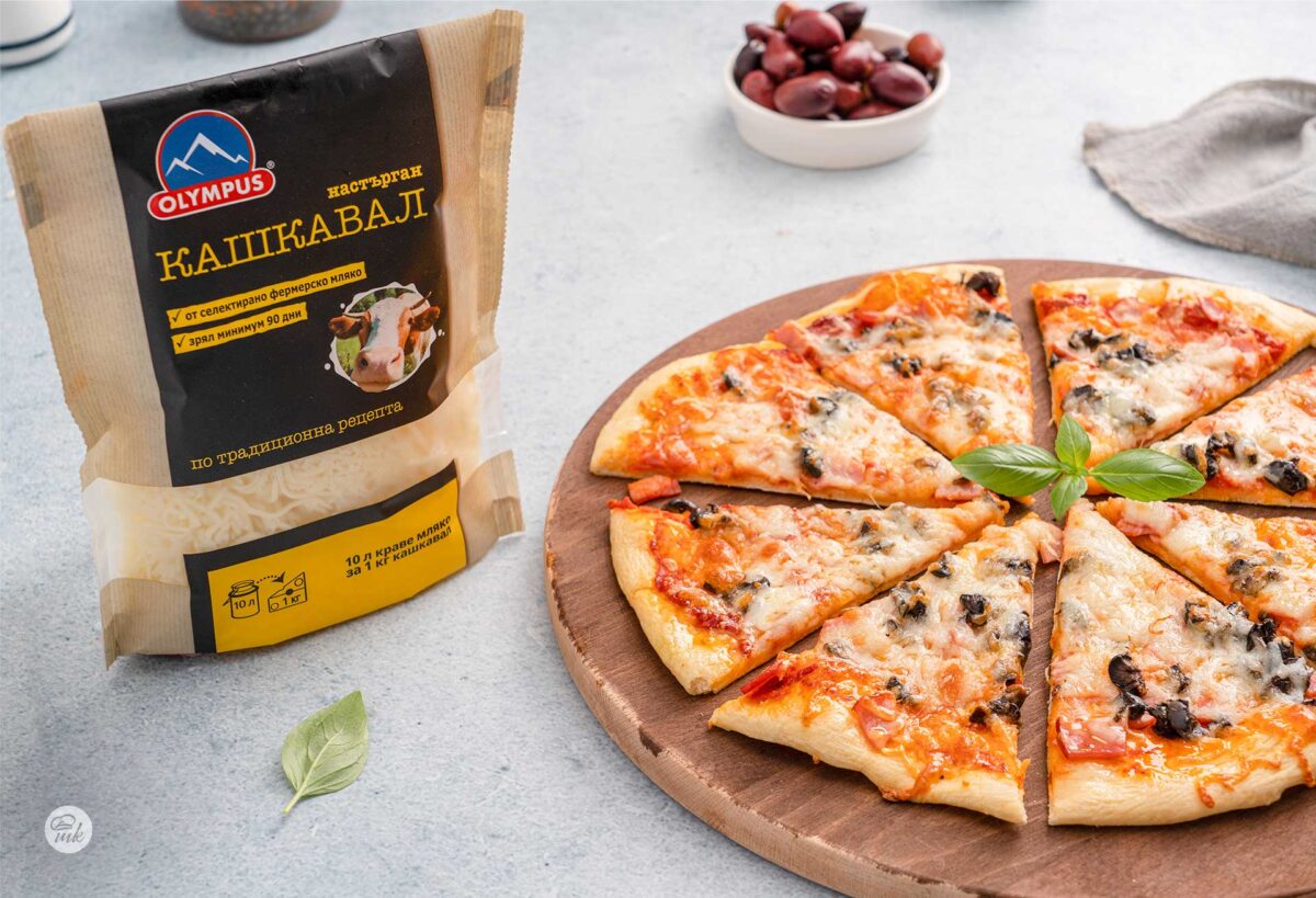 Пица "Капричоза" с настърган кашкавал Olympus, нарязана на парчета с пакет кашкавал до нея, снимано отстрани