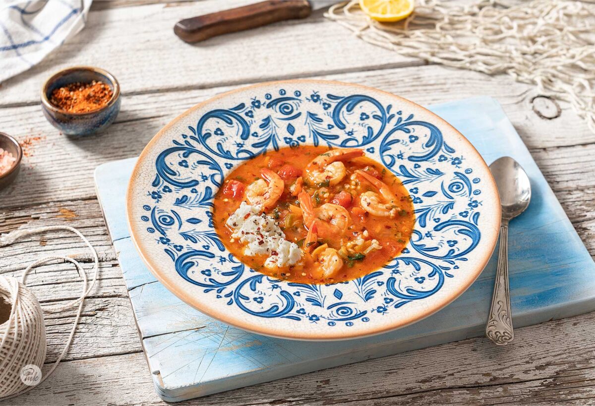 Супа от скариди, домати и чесън, сервирана в дълбока чиния на синя дъска, снимана отстрани