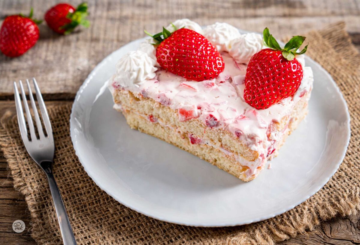 Квадратно парче ягодова торта с бишкоти в бяла чинийка, снимано отстрани