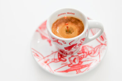 Чаша кафе в бяла чашка с червени мотиви върху чинийка, снимано под ъгъл