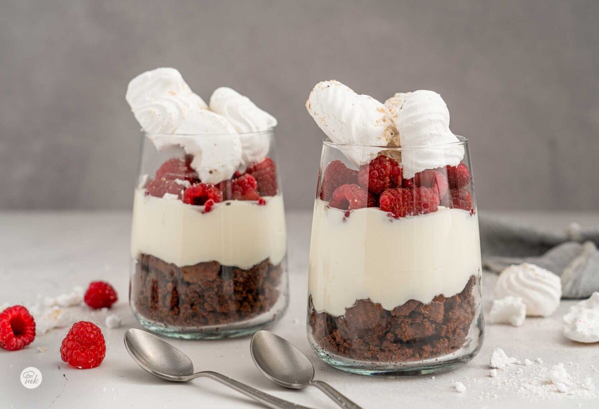 Две чаши бисквитен десерт с малини, снимани отпред