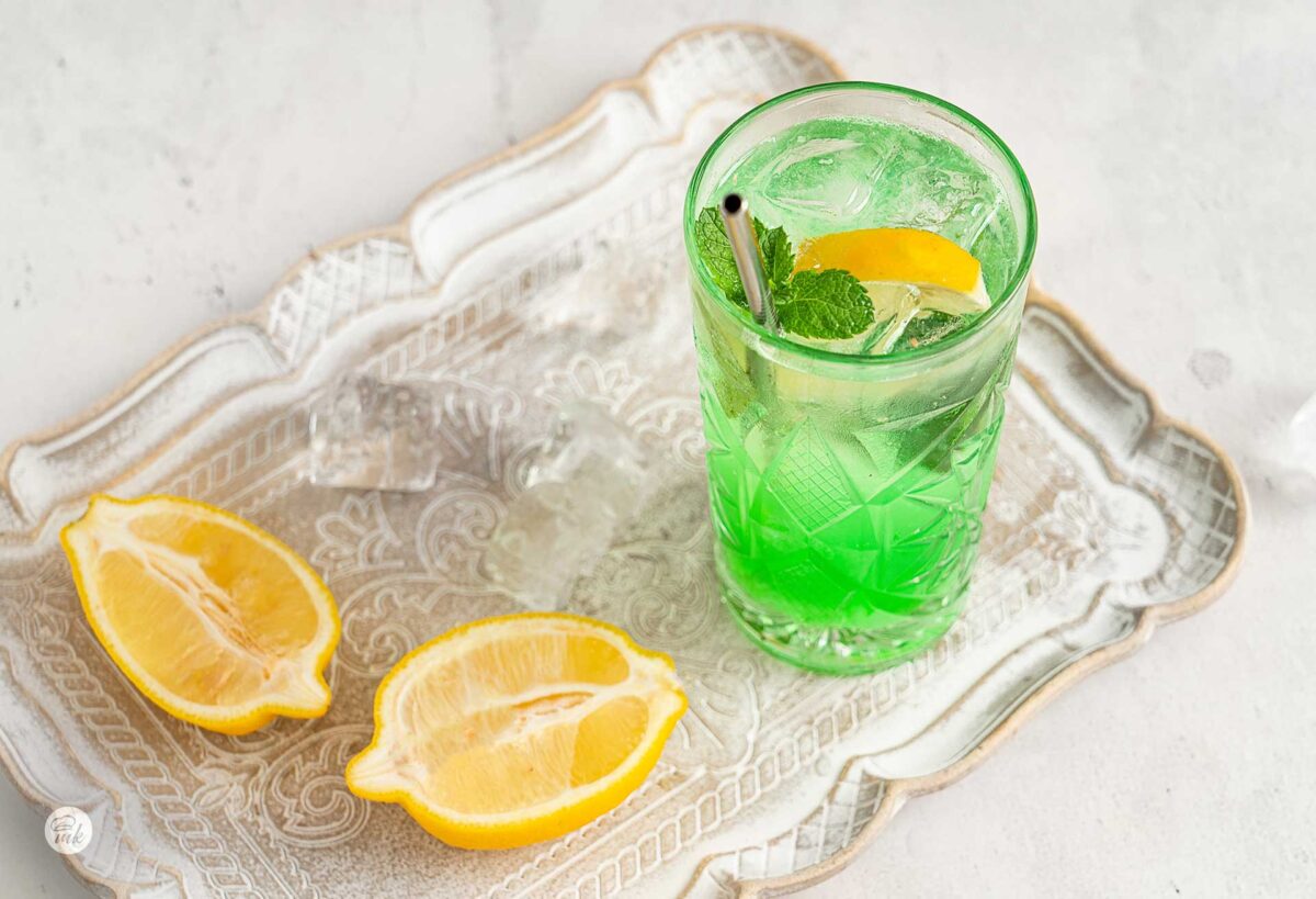 Чаша домашна лимонада с мента и срязан лимон до нея, снимани от горен десен ъгъл