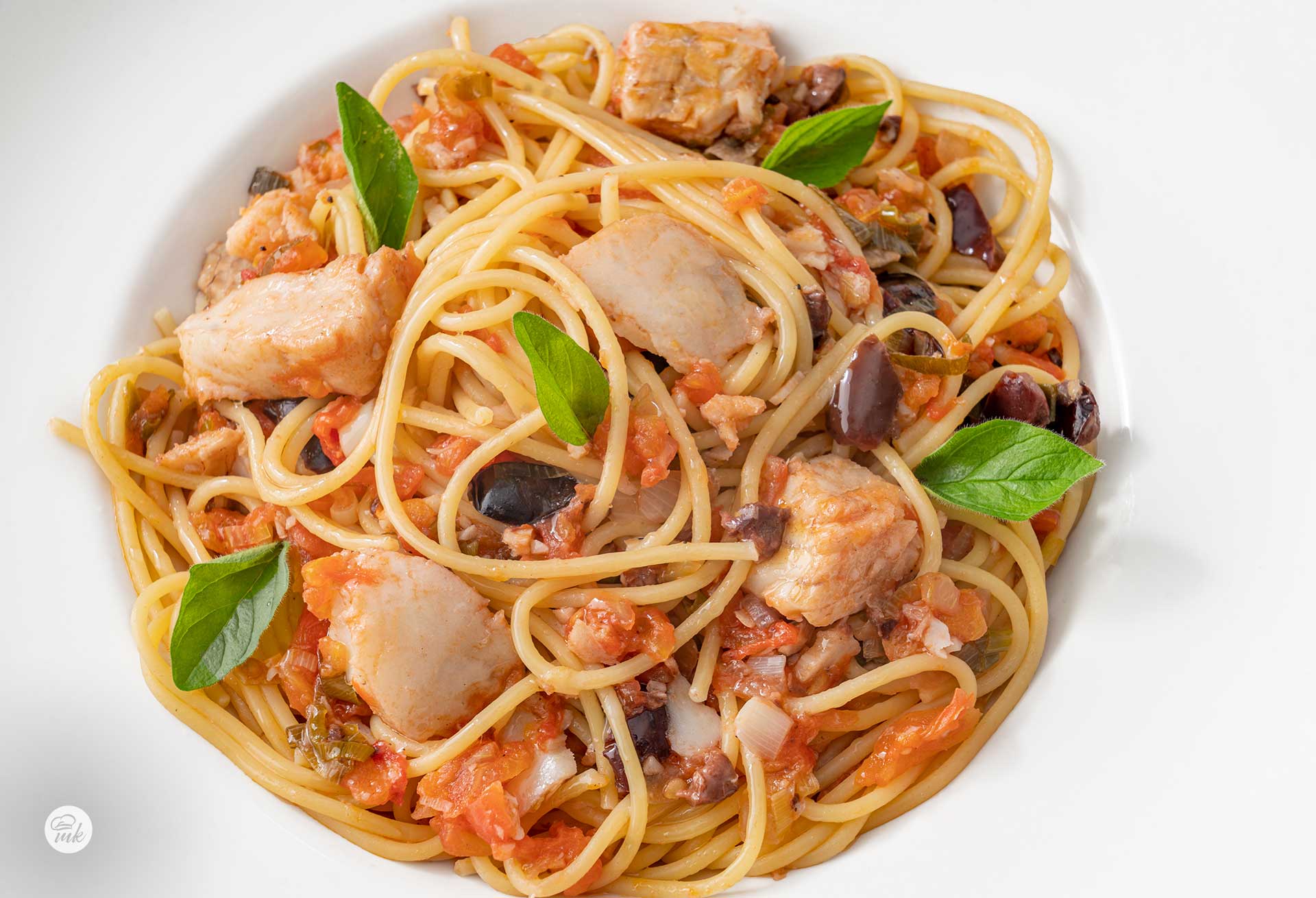 Спагети с риба, домати и маслини в бяла чиния, снимани отгоре