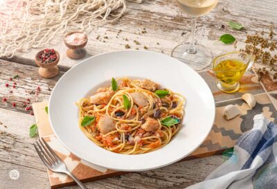 Спагети с риба, домати и маслини в бяла чиния, снимани отдясно