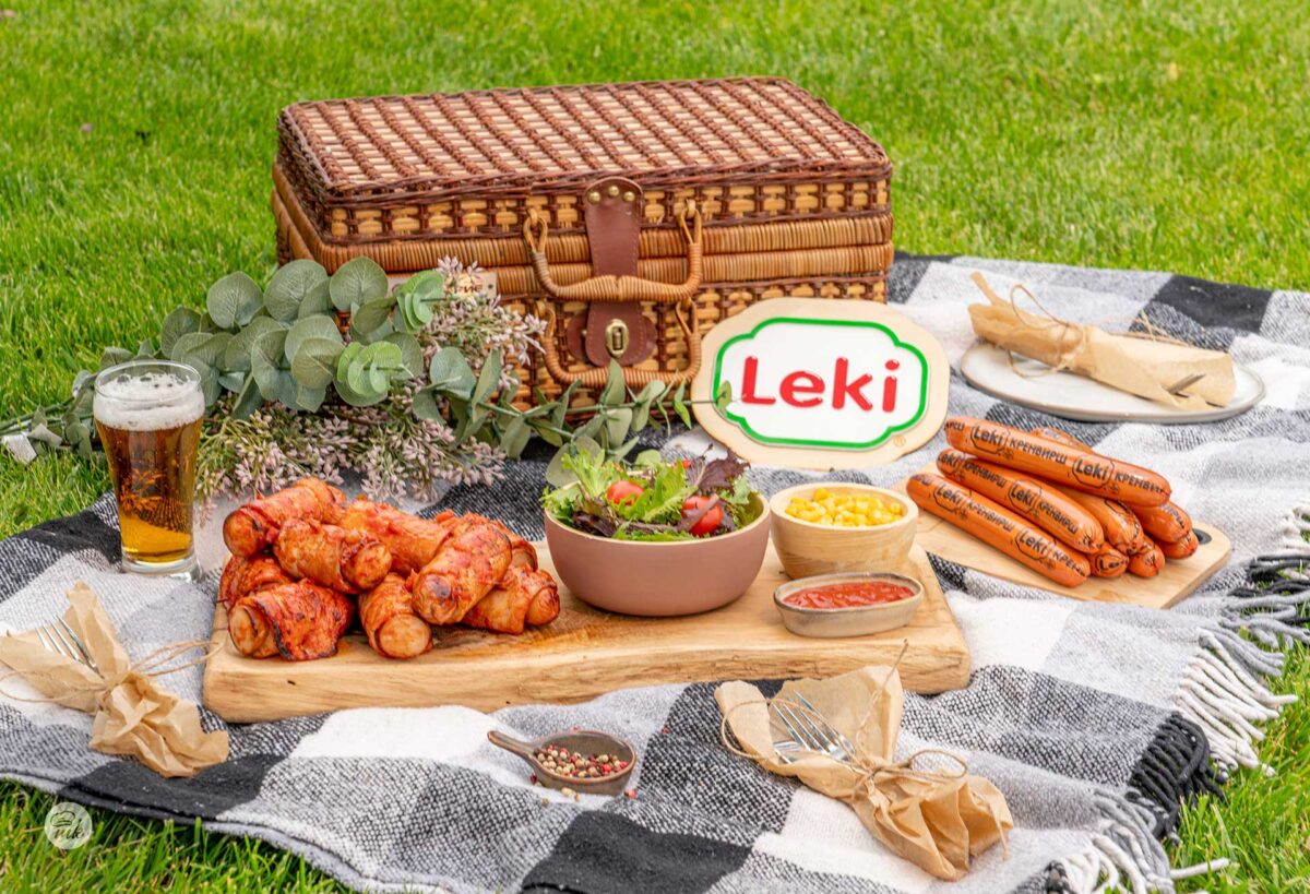 Кренвирши Leki с бекон и барбекю сос върху дървена дъска на тревата, снимани отпред