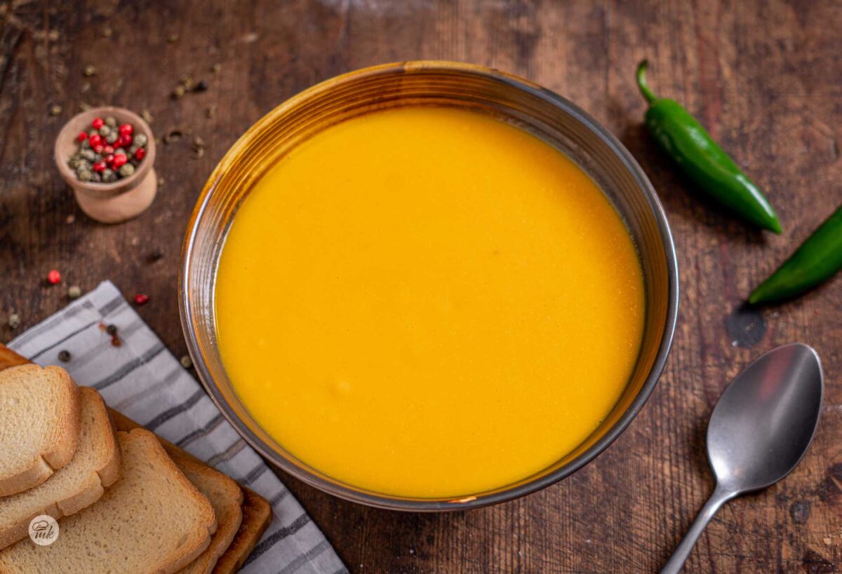 Купичка крем супа от червена леща и моркови, до нея сухари и пресни зелени люти чушки