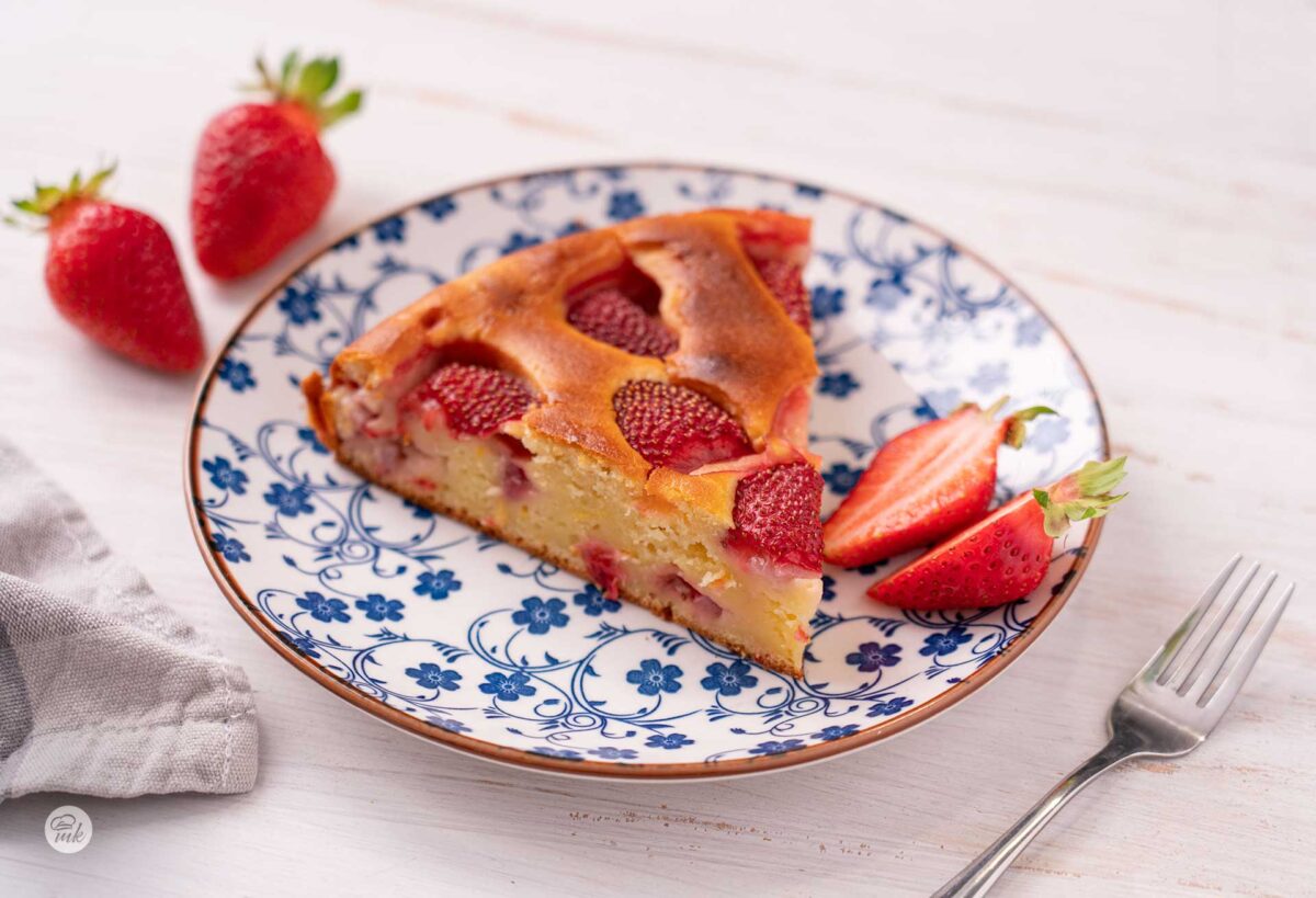 Триъгълно парче сладкиш с ягоди в десертна чинийка и срязана на две ягода до него