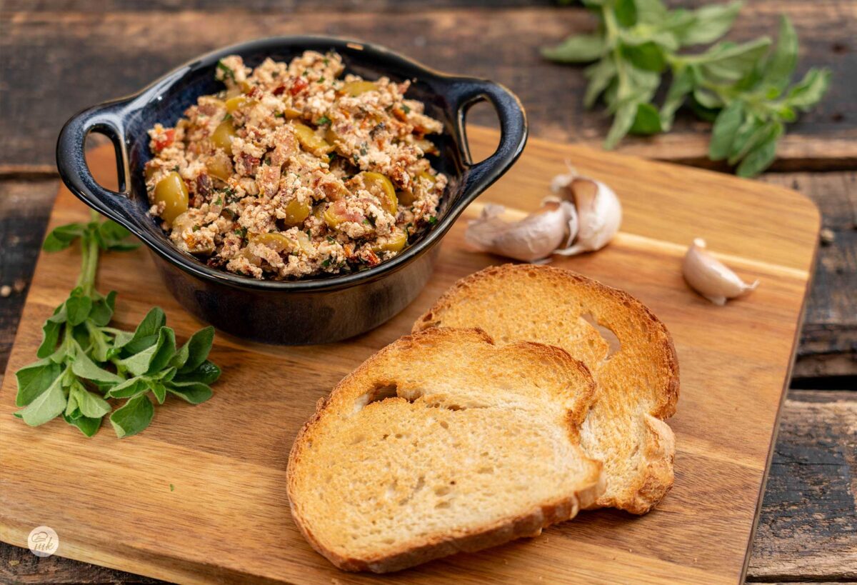 Разядка с печено сирене, маслини и сушени домати в купичка и до нея две филийки препечен хляб