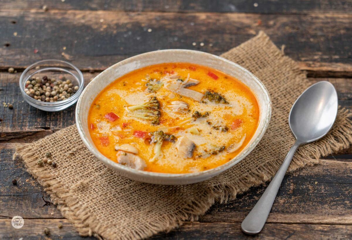 Зеленчукова супа от броколи и гъби в порцеланова купа, до която има метална лъжица и малка купичка с цветен черен пипер
